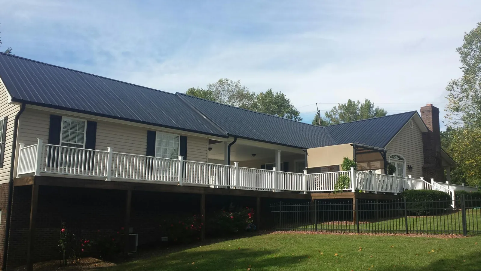 Black metal roof above a long white railed deck on a hillside home in Albion
